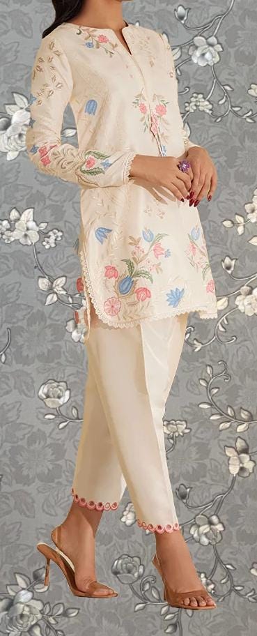 A woman wearing a white dress with floral embroidery and high heels stands against a gray floral background.