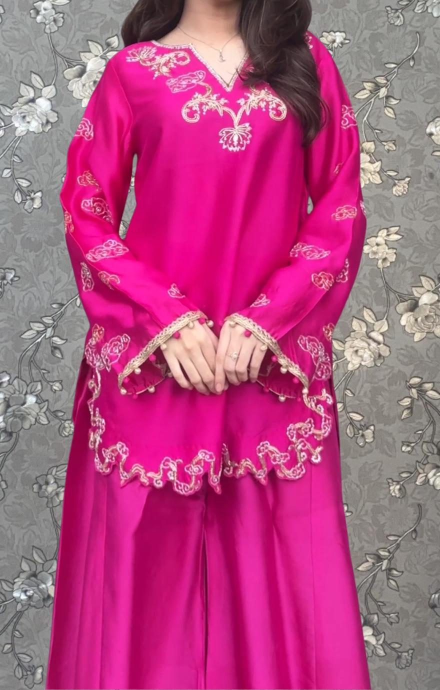 A woman wearing a bright pink dress with intricate embroidery and a high collar.