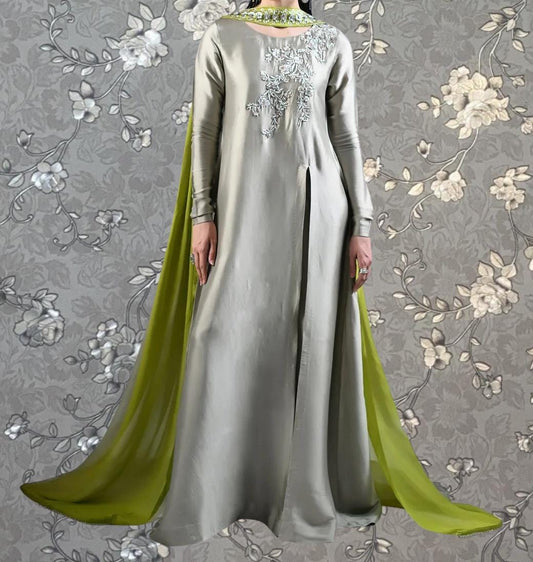 A person wearing a long, gray dress with green accents, standing against a gray floral background.