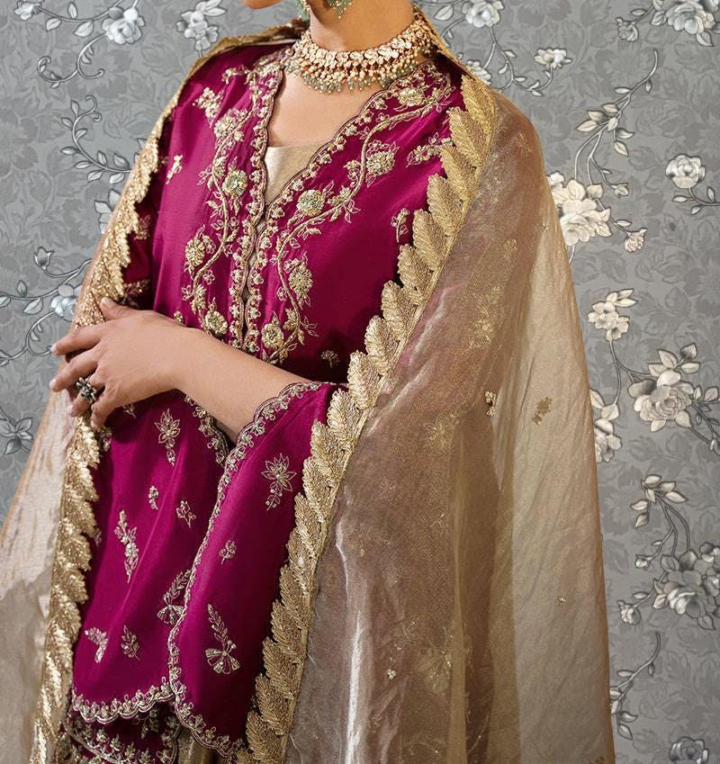 A woman wearing a vibrant pink and gold dress with intricate embroidery and a matching gold and beige shawl.