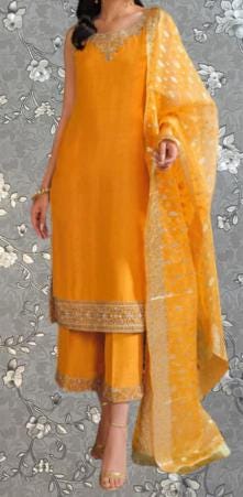 A woman wearing a bright yellow dress with a matching yellow shawl, standing against a gray floral background.