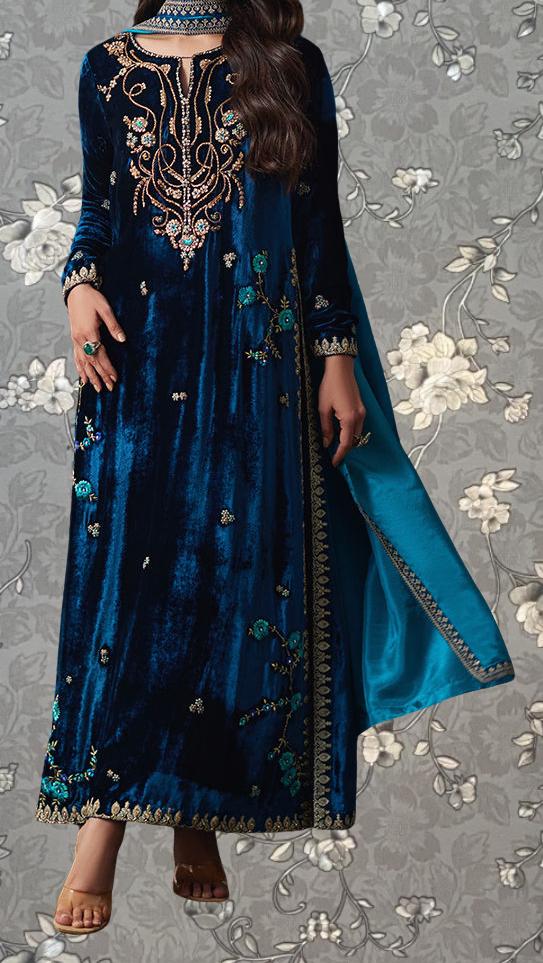 A woman wearing a long, blue velvet dress with intricate embroidery and floral designs.