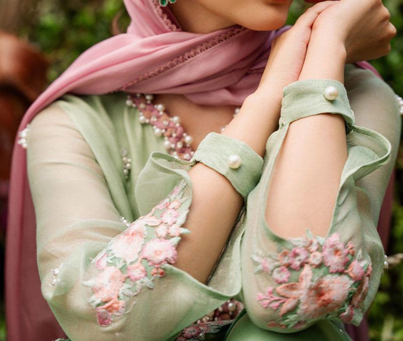 A close-up of a person wearing a green dress with pink floral embroidery, and a pink scarf draped over their head.