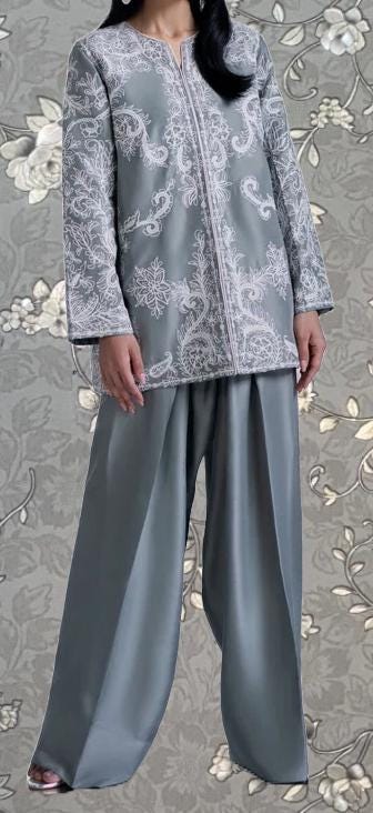A person wearing a gray and white patterned jacket and wide-leg pants stands against a gray floral background.