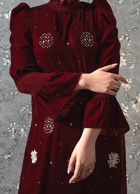 A close-up of a person wearing a red dress with white floral embroidery, posing with their arms crossed.