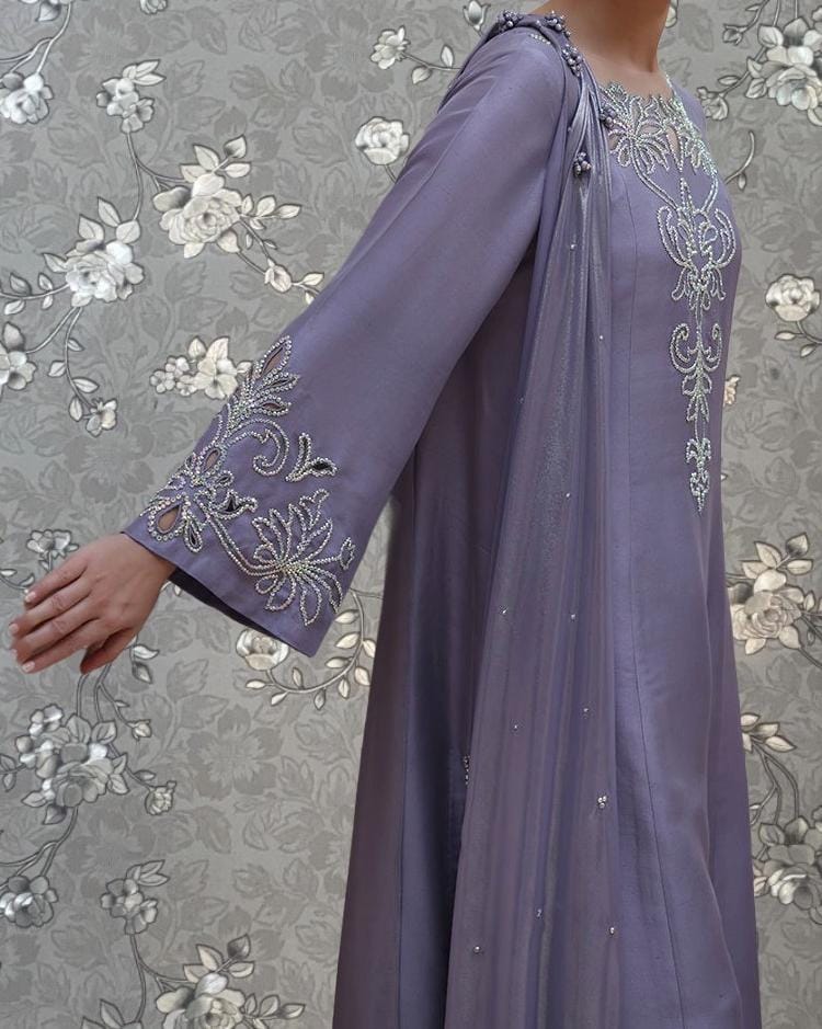 A person wearing a long, purple dress with intricate embroidered designs on the sleeves and a flowing, draped skirt.