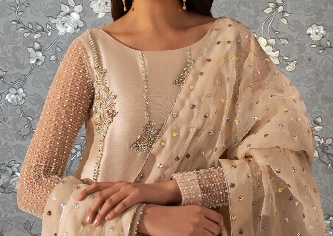 A close-up of a woman wearing a beige dress with intricate embroidery and a sheer, polka-dotted shawl.