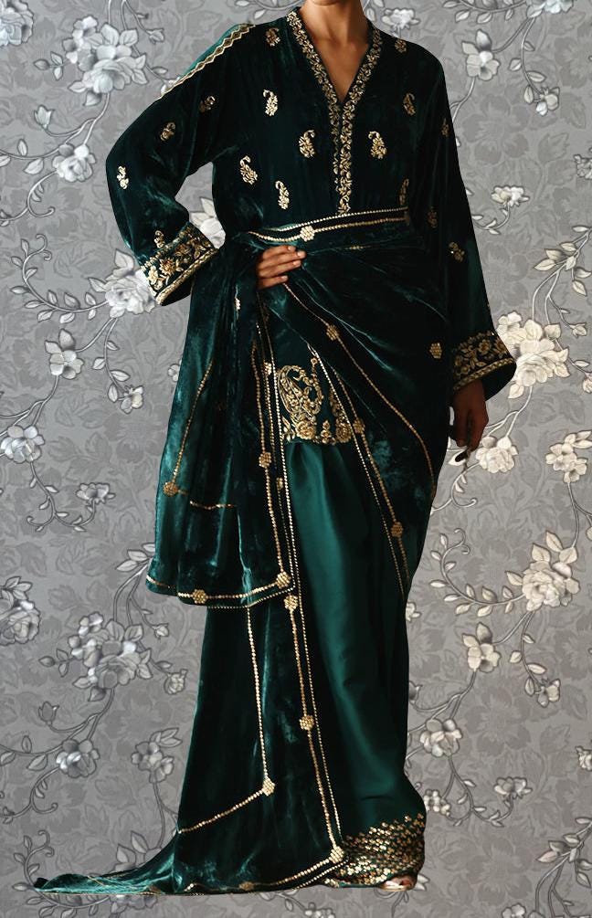 A person wearing a long, green velvet dress with gold embroidery and a matching green and gold sash.