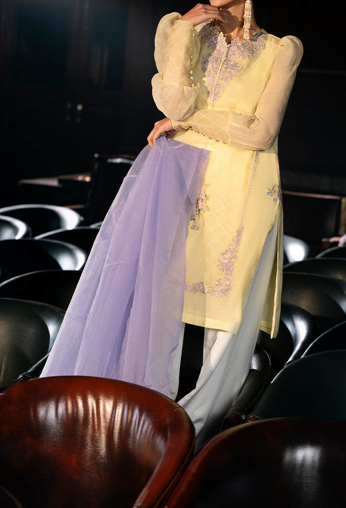 A woman in a yellow dress with a purple shawl stands in a room with rows of chairs.