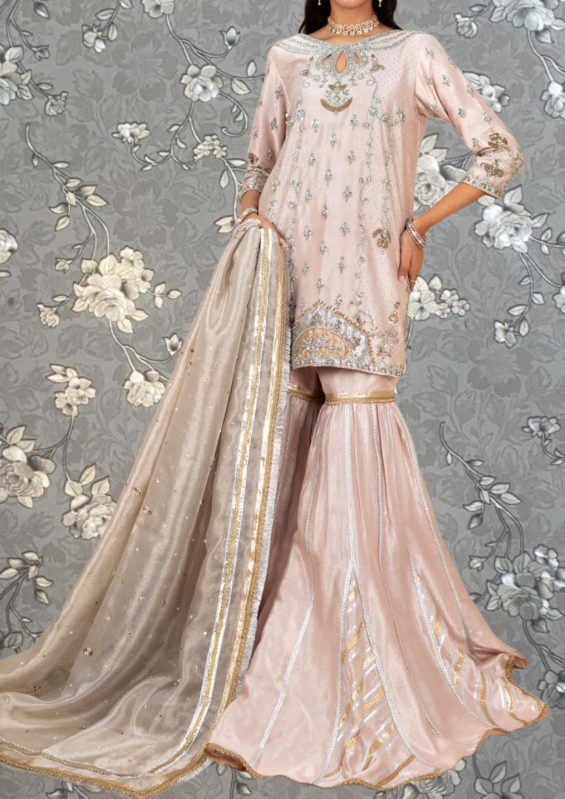 A woman wearing a pink and gold dress with a long train, standing against a gray floral background.