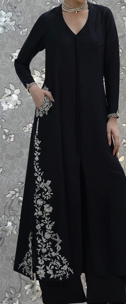 A person wearing a long black dress with intricate white embroidery on the side.