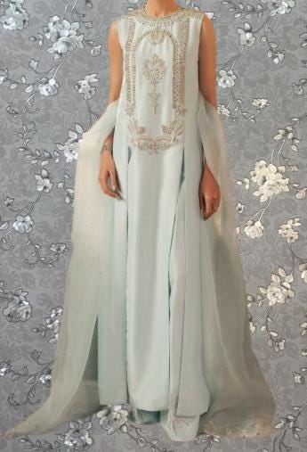 A woman wearing a long, light blue dress with intricate embroidery and a flowing, draped skirt.