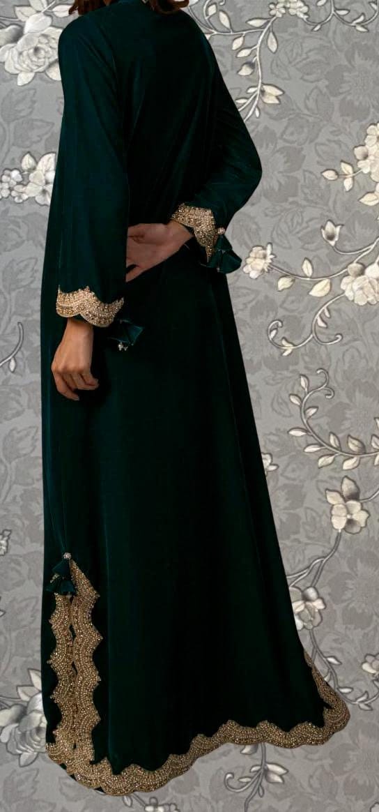 A person wearing a long, dark green dress with gold embroidery and a matching gold trim along the bottom edge.