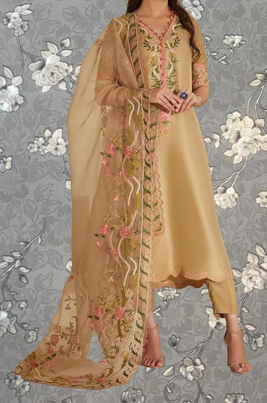 A woman wearing a gold and beige dress with intricate floral embroidery, standing against a gray floral background.