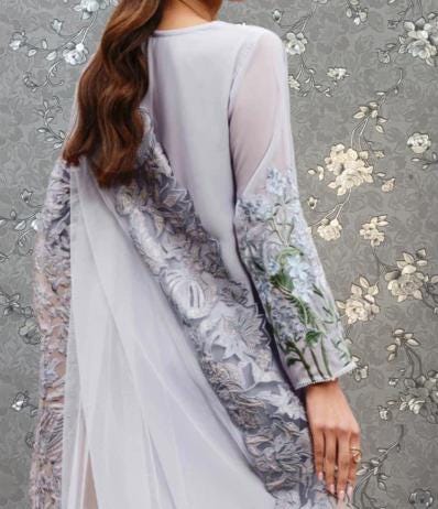 A woman wearing a long, flowing gray dress with intricate floral embroidery on the sleeves and back.