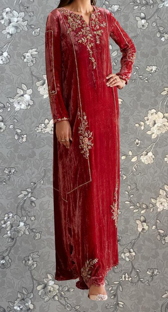 A woman wearing a long, red velvet dress with intricate embroidery and floral patterns.
