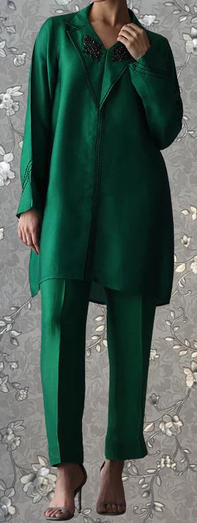 A person wearing a green dress and matching green pants stands against a gray floral background.