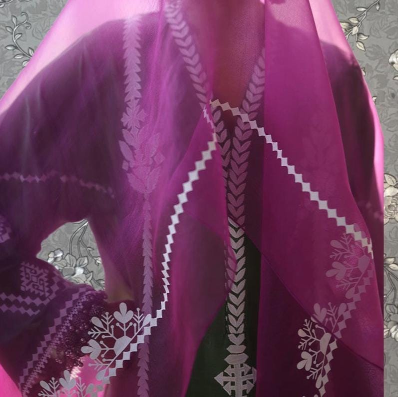 A close-up view of a person wearing a purple dress with intricate white embroidery.