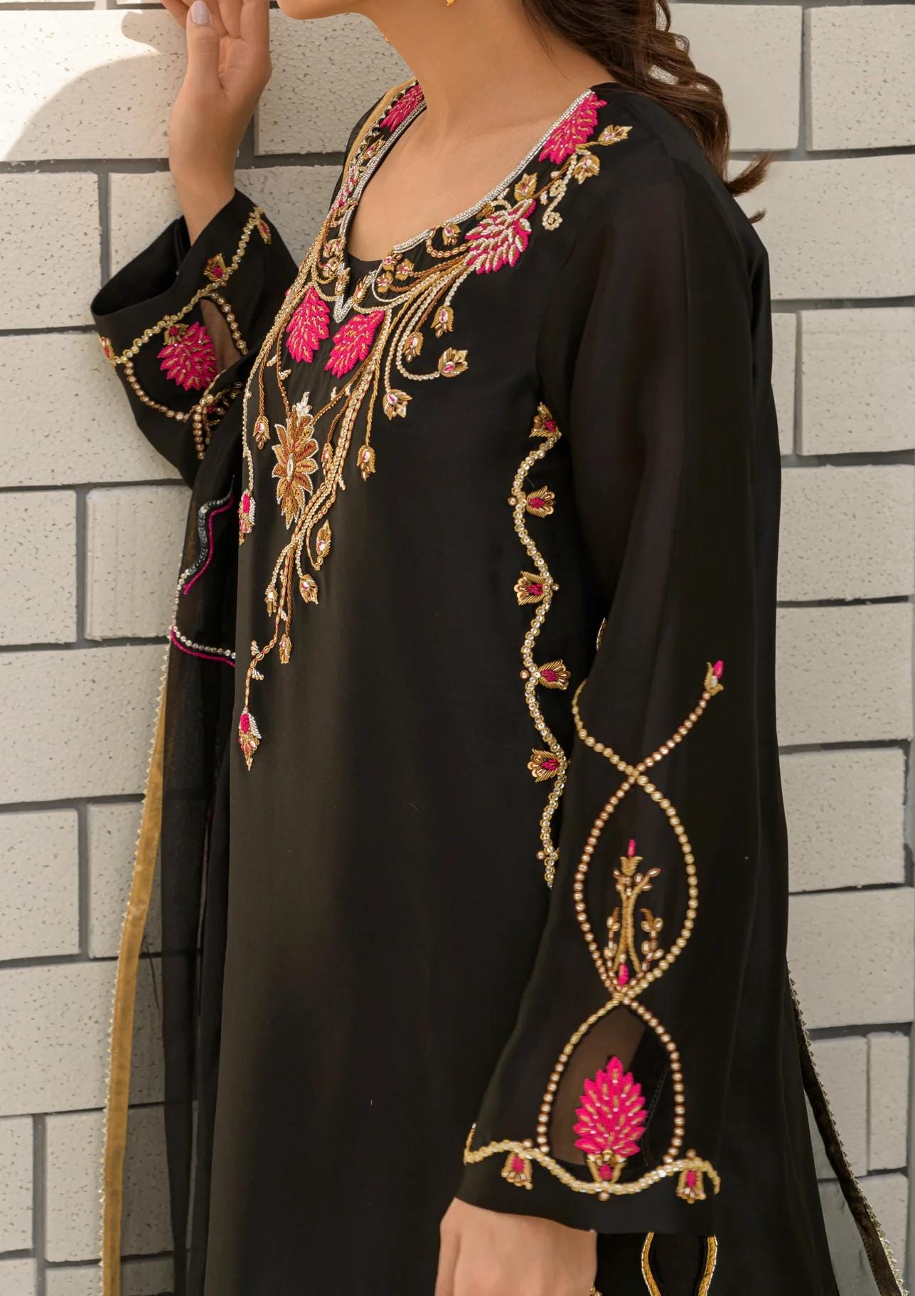 A woman wearing a black dress with intricate embroidered designs in pink and gold.