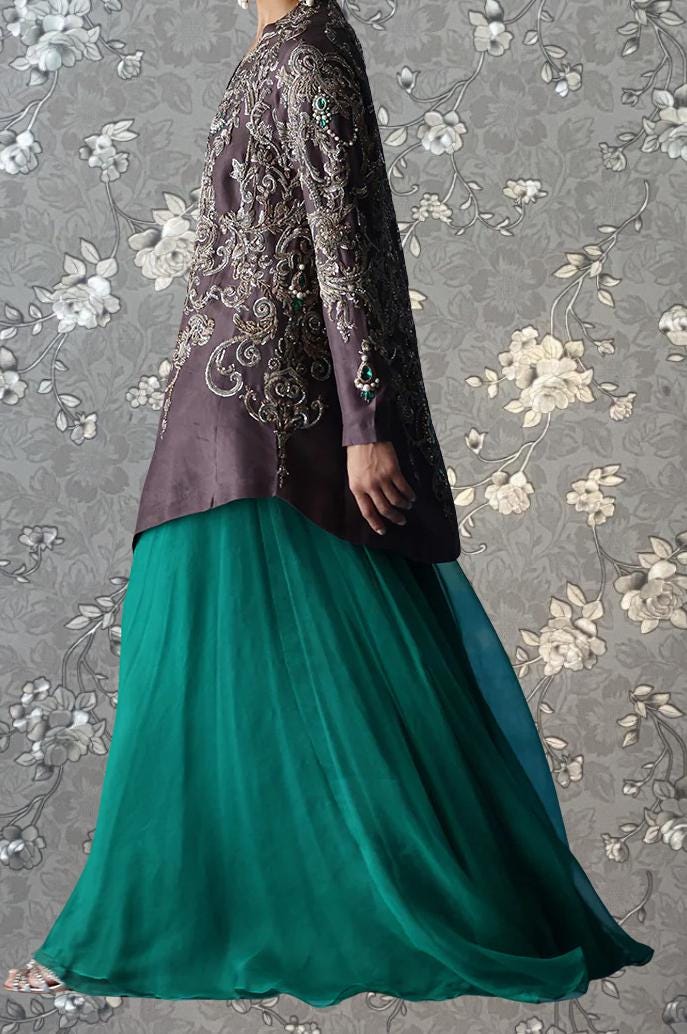 A person wearing a long, purple jacket with intricate embroidery and a long, green skirt.