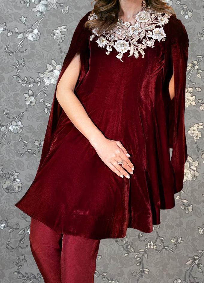 A woman wearing a red velvet dress with a floral pattern and a cape-like design on the neckline.