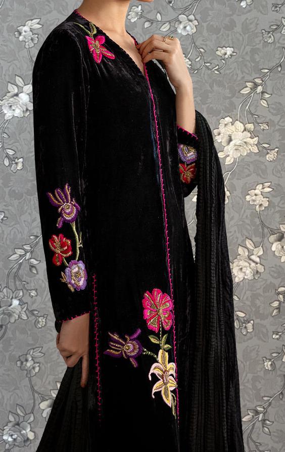 A person wearing a long black dress with colorful floral embroidery on the sleeves and collar.