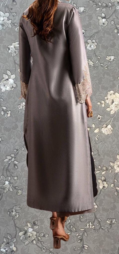 a person wearing a long gray coat with lace sleeves, standing against a gray floral background.
