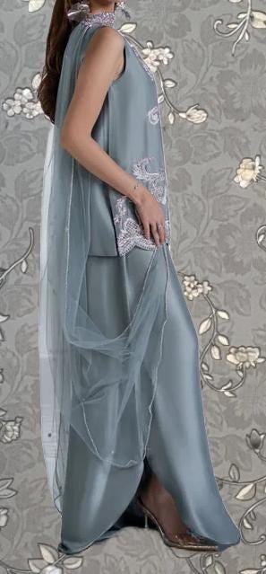 A woman wearing a long, gray dress with a sheer, flowing skirt and a matching sheer cape draped over her shoulders.
