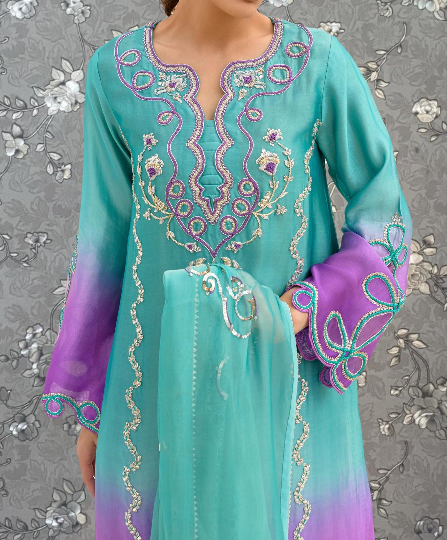 A woman wearing a turquoise and purple dress with intricate embroidered patterns on the front.