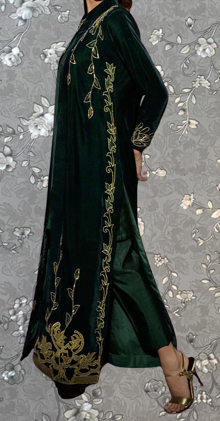 A person wearing a long, green velvet dress with gold embroidered patterns on the sleeves and hem.