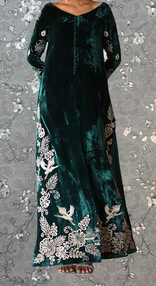 A woman wearing a long, green velvet dress with intricate floral embroidery on the bodice and skirt.