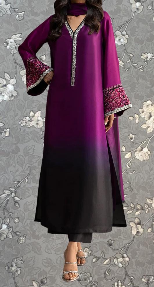 A woman wearing a long purple dress with a black and purple patterned design, standing against a gray floral background.