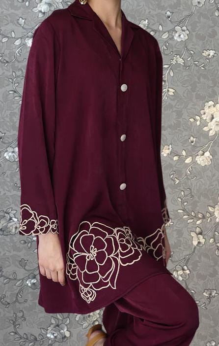 A person wearing a burgundy dress with white floral embroidery on the sleeves and hem.