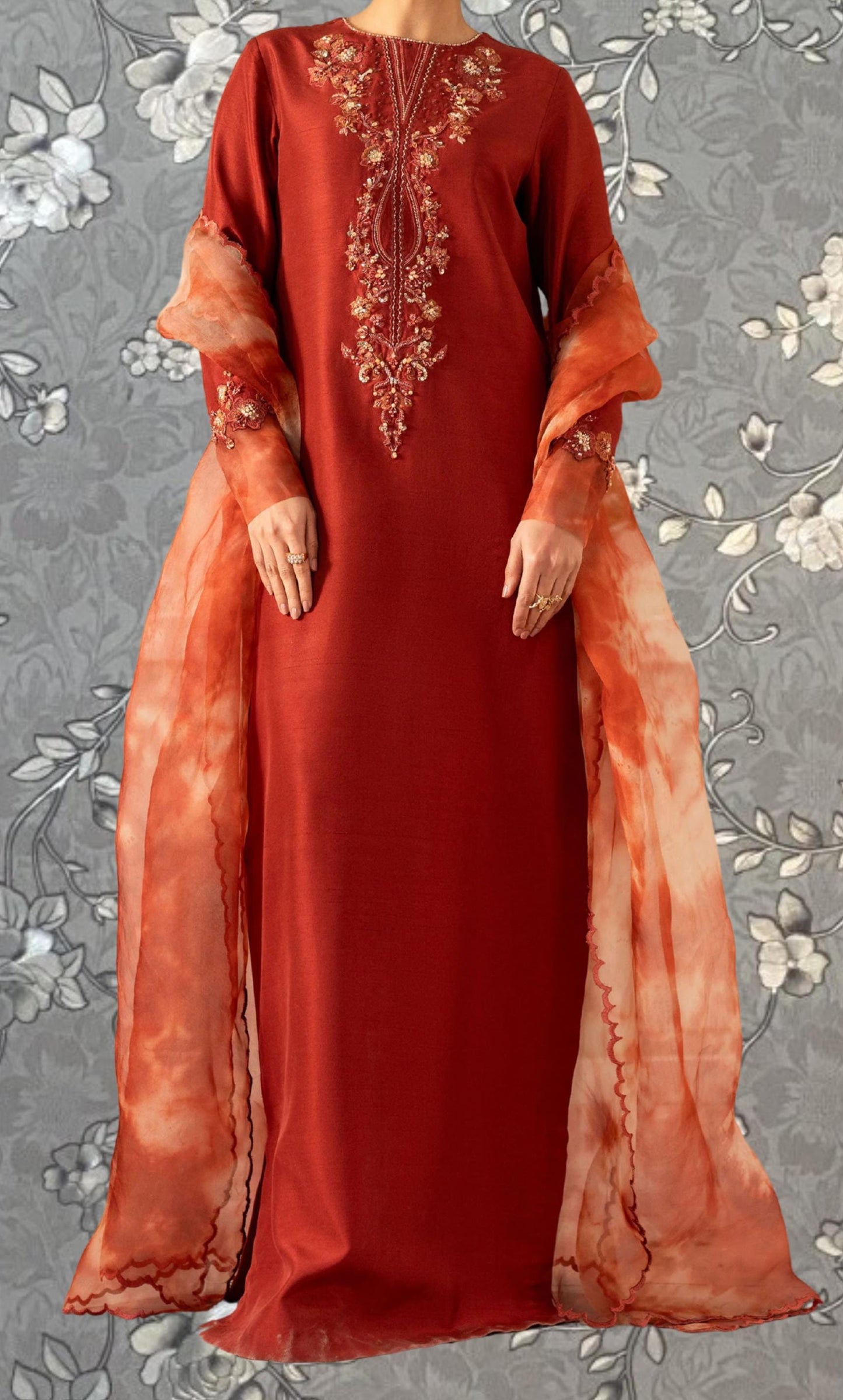 A woman wearing a long red dress with intricate embroidery and a flowing orange shawl.