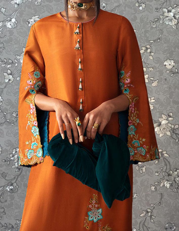 A person wearing an orange dress with floral embroidery and holding a green garment.