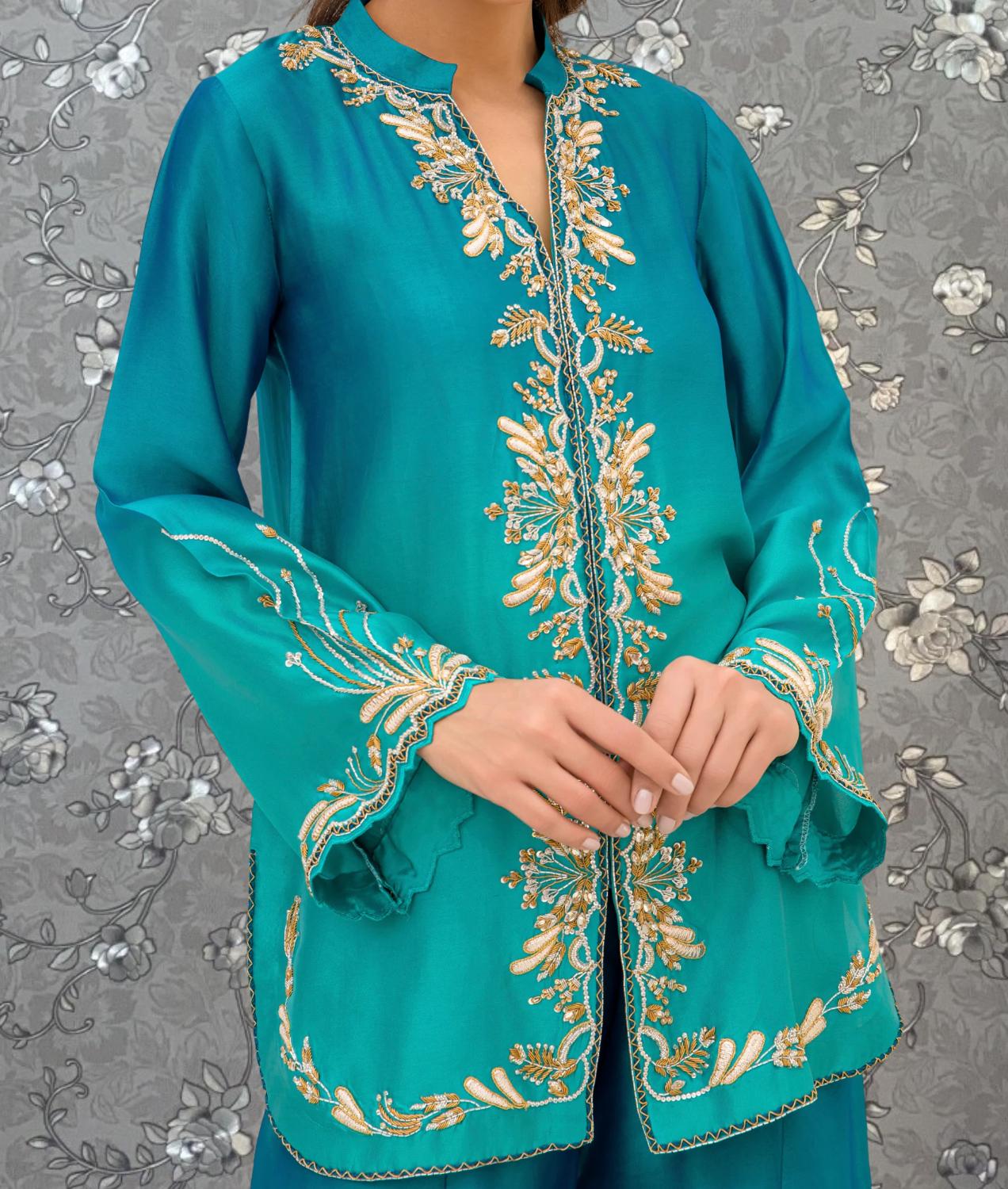 A woman wearing a teal-colored dress with intricate gold embroidery on the sleeves and collar.