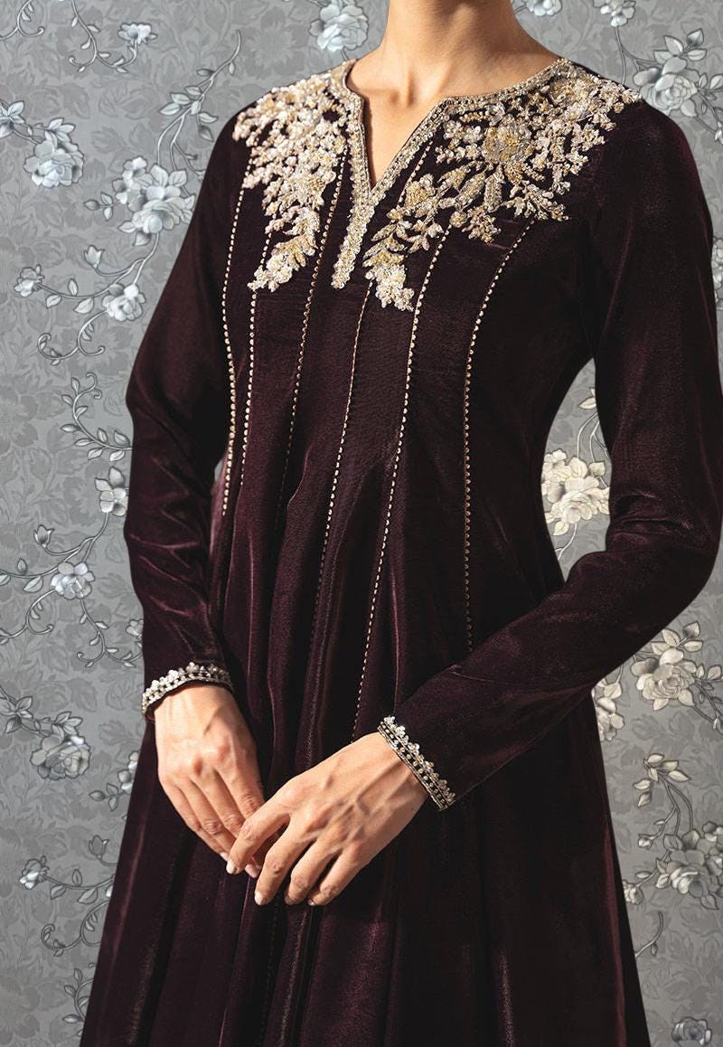 A woman wearing a long, burgundy velvet dress with intricate gold embroidery on the neckline and sleeves.