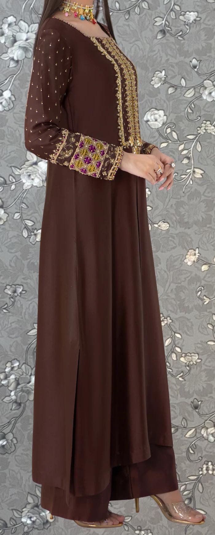 A woman wearing a brown dress with gold embroidery and a floral pattern on the background.