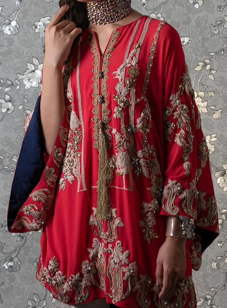 A woman wearing a vibrant red dress with intricate gold embroidery and a matching gold necklace.