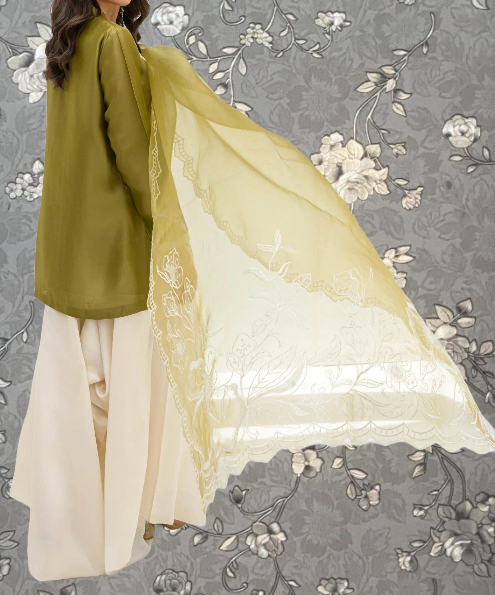 A woman wearing a green blouse and white skirt is holding a yellow and white fabric with floral designs.