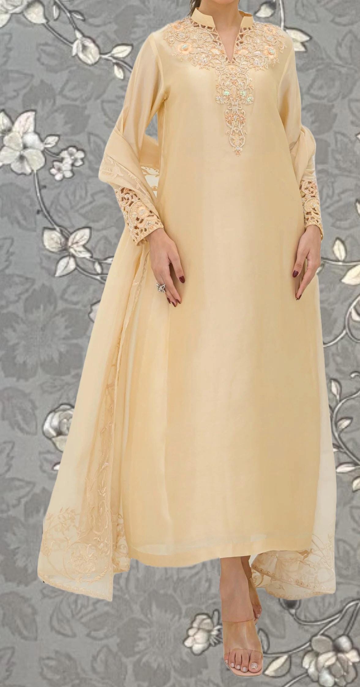 A woman wearing a long, cream-colored dress with intricate embroidery and lace details.
