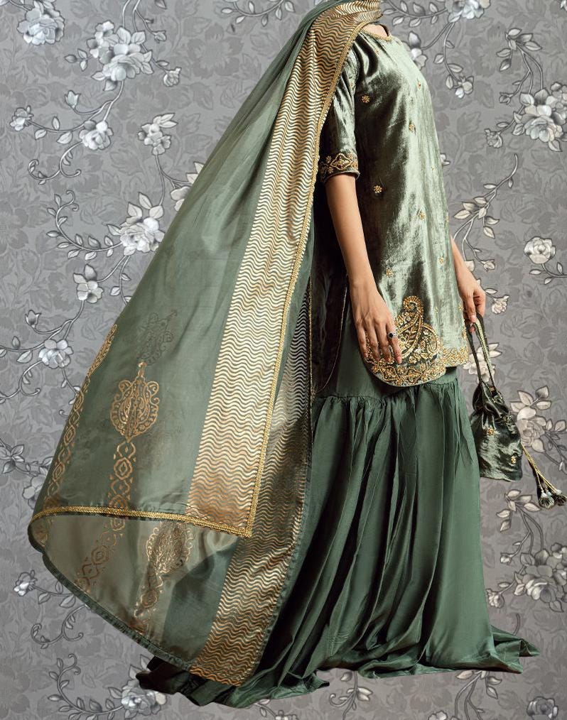 A woman wearing a green and gold dress with a long, flowing skirt and a matching green shawl draped over her shoulders. She is holding a small purse in her hand.