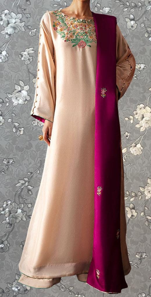 A woman wearing a long, light pink dress with a floral embroidered design on the front. She is also wearing a long, purple shawl with small floral embroidery. The background features a gray floral pattern.