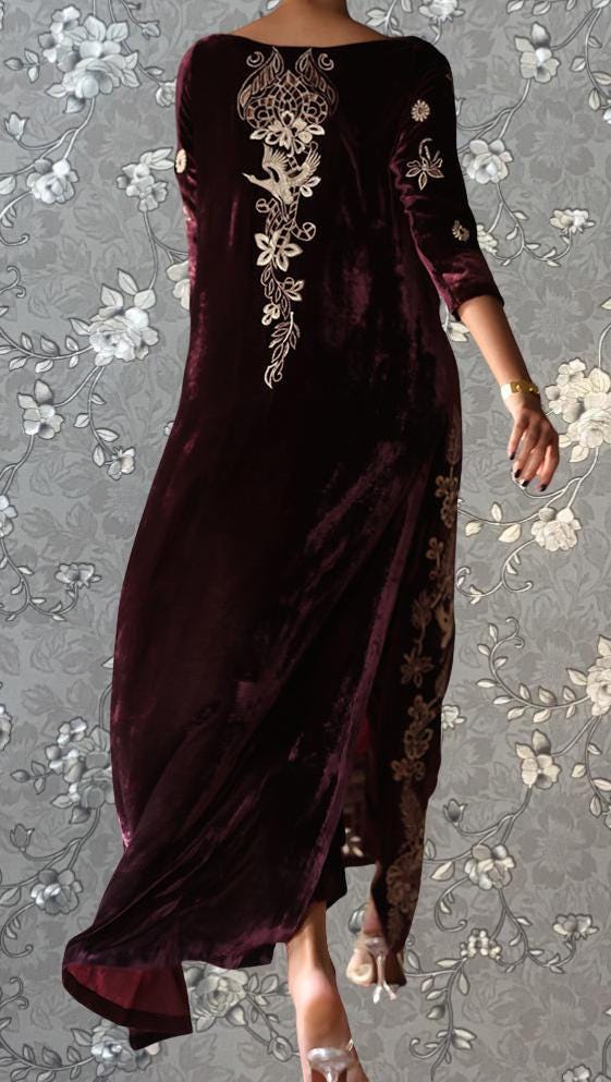 A woman wearing a long, burgundy velvet dress with intricate floral embroidery on the back.
