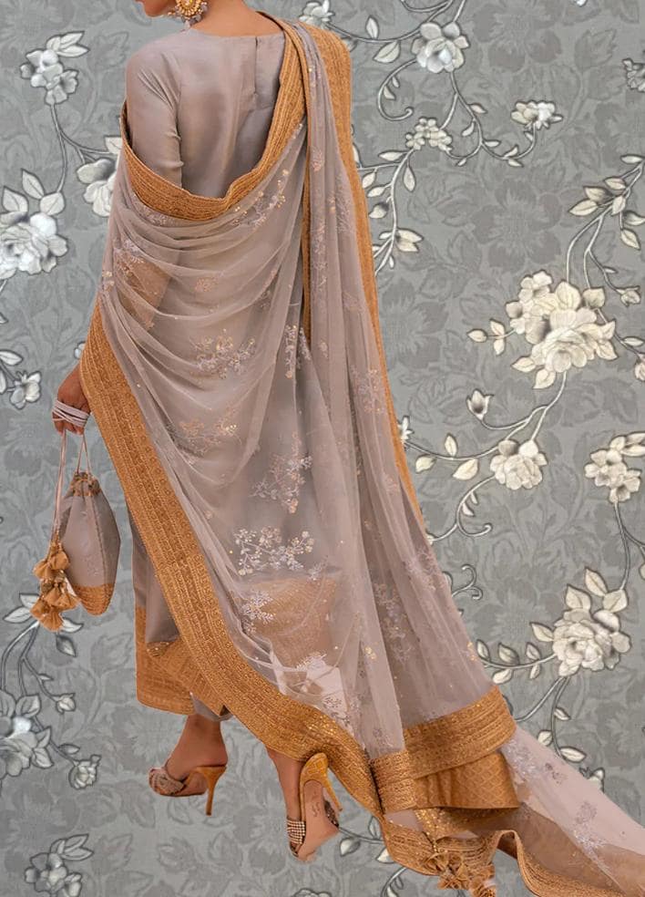 A woman wearing a gray and gold dress with a long, flowing skirt and a matching shawl, standing against a gray floral background.