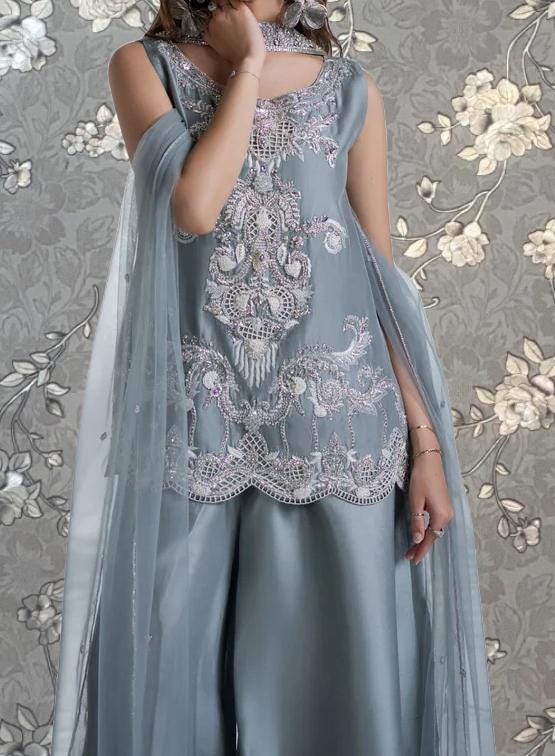 A woman wearing a gray dress with intricate embroidery and a flowing gray shawl.