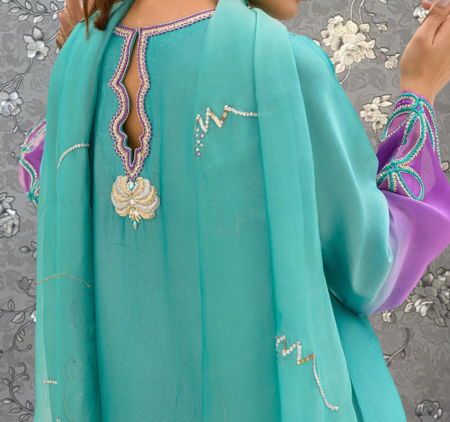 a close-up view of a person wearing a turquoise dress with a purple and teal patterned sleeve. The dress has a decorative back opening and a matching turquoise scarf draped over the shoulder.