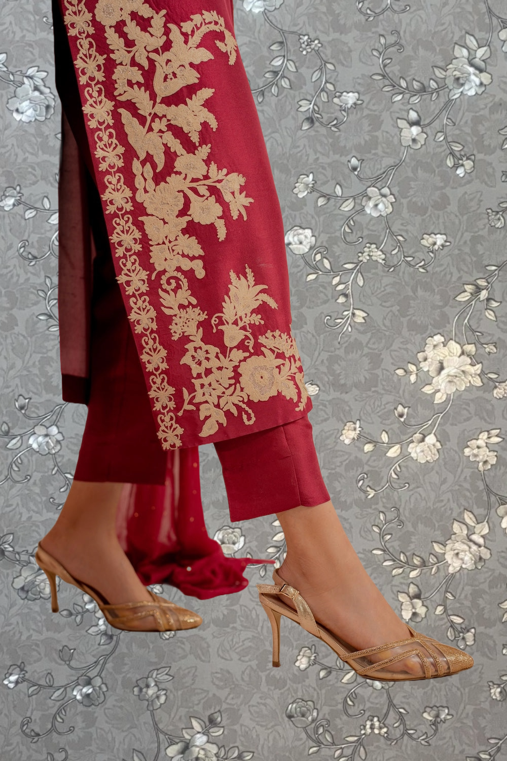 A close-up of a person wearing a red and gold embroidered dress, with gold high heels visible.
