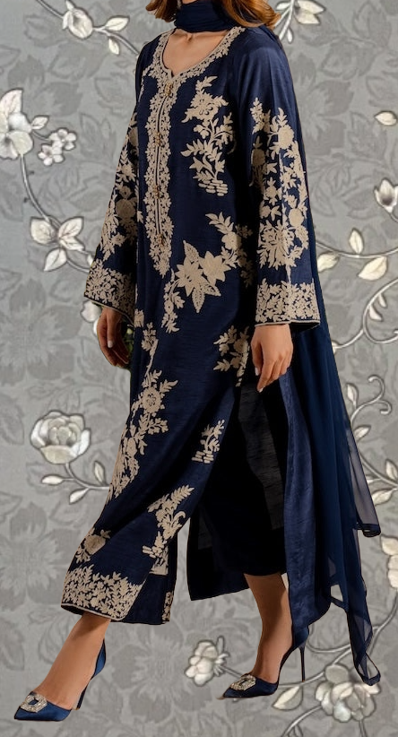 A woman wearing a long navy blue dress with gold embroidered patterns, standing against a gray floral background.