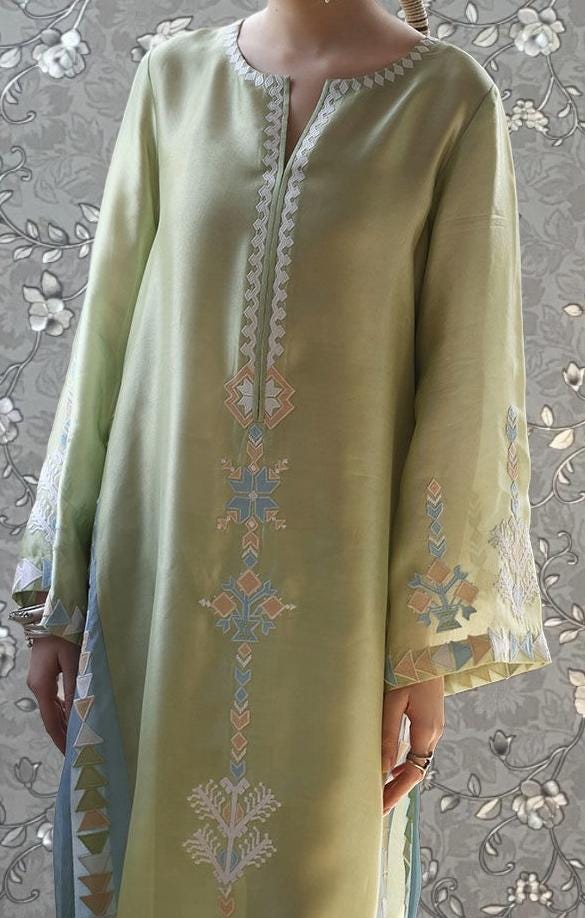 A person wearing a long, green dress with intricate embroidered patterns on the front.